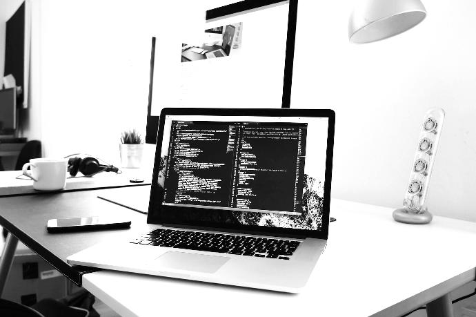 A MacBook with lines of code on its screen on a busy desk